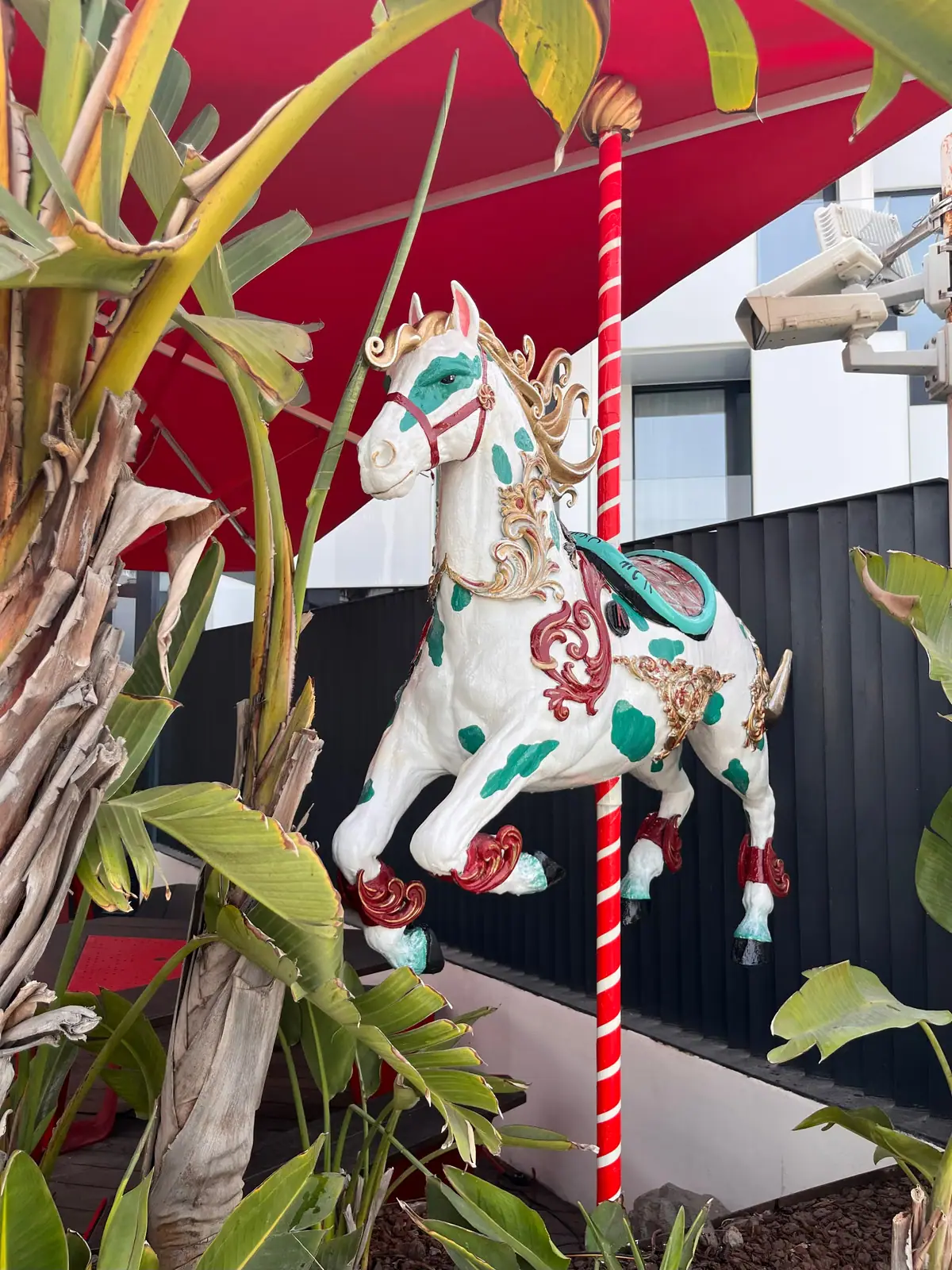 Caballo de carrusel blanco con manchas verdes y adornos dorados en la terraza de Arrogante
