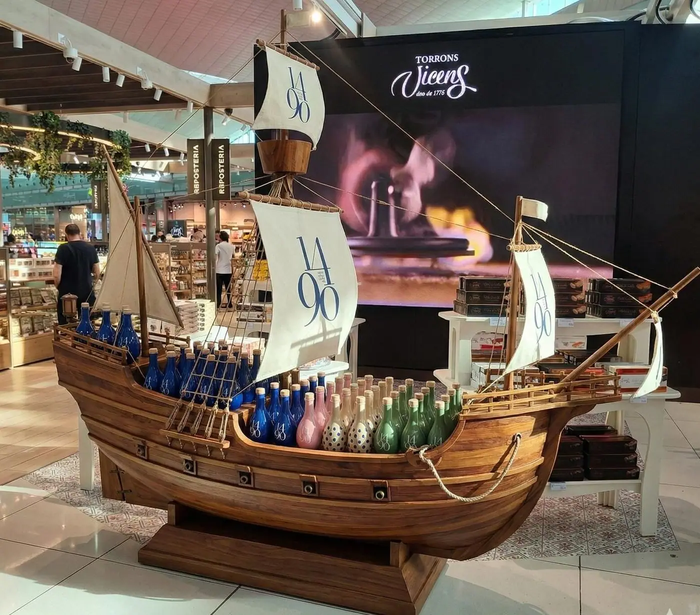 Barco corpóreo de gran formato con velas y botellas en la cubierta, en una tienda
