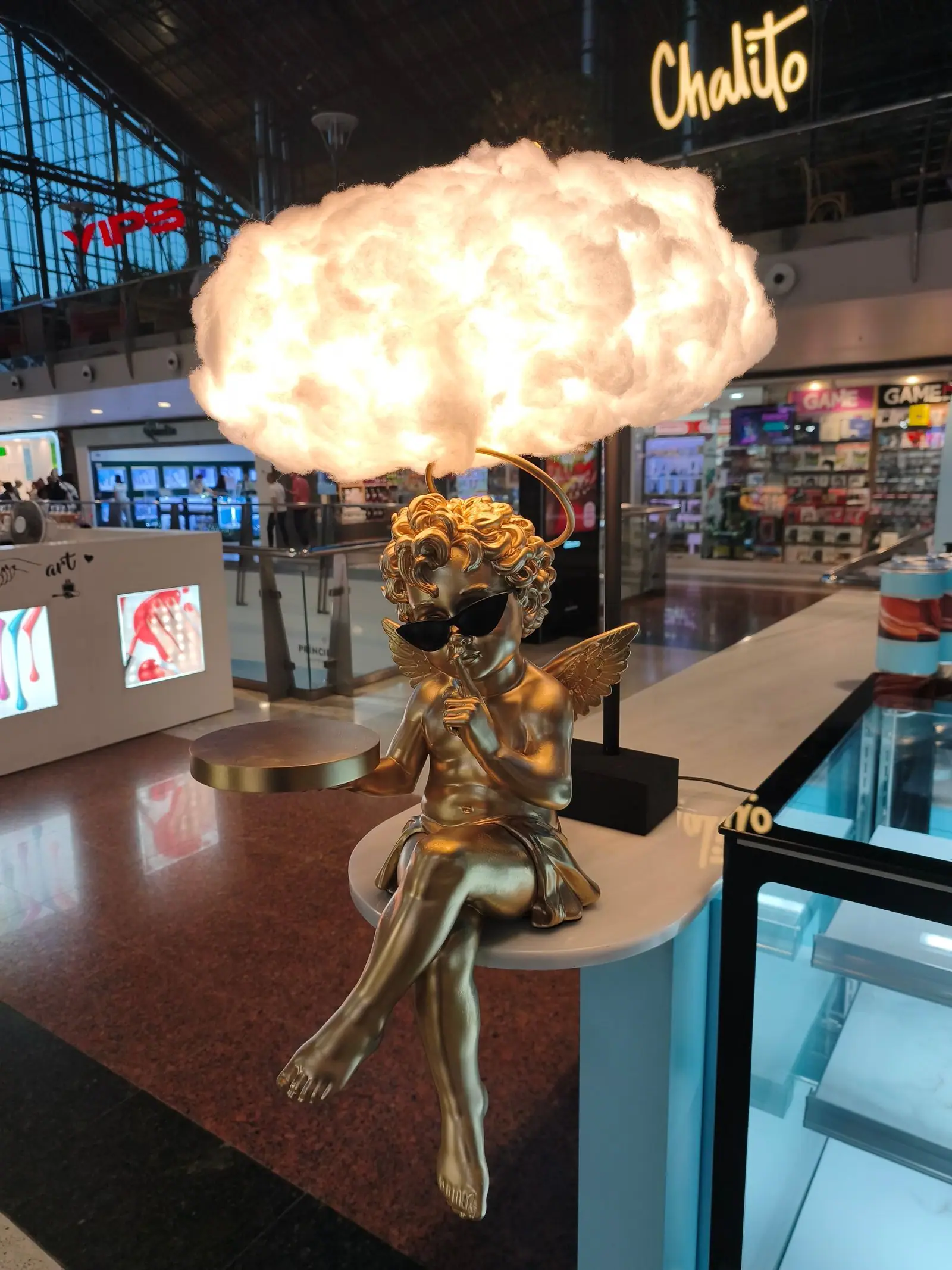 El cupido con su nube encendida en el mostrador, con el centro comercial detrás