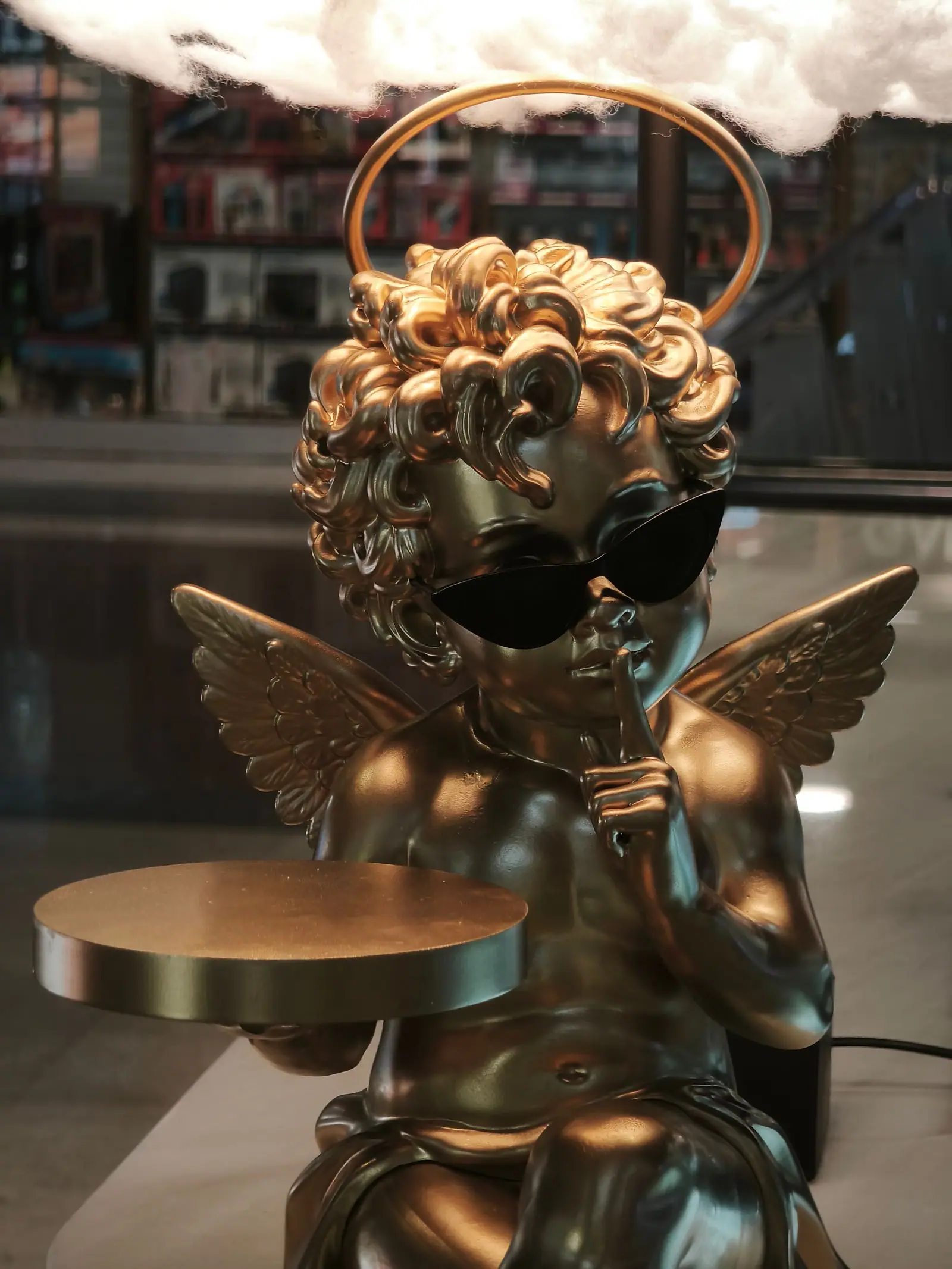 El cupido dorado sujetando la bandeja, con la aureola y las gafas de sol