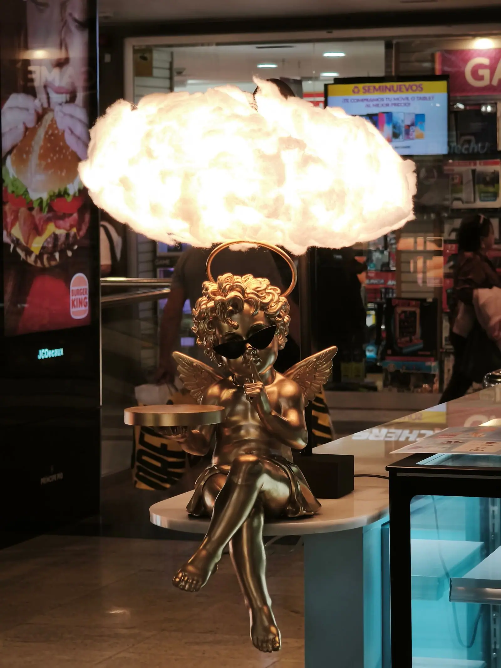 Cupido dorado con gafas de sol bajo una nube de luz, en la decoración de un centro comercial