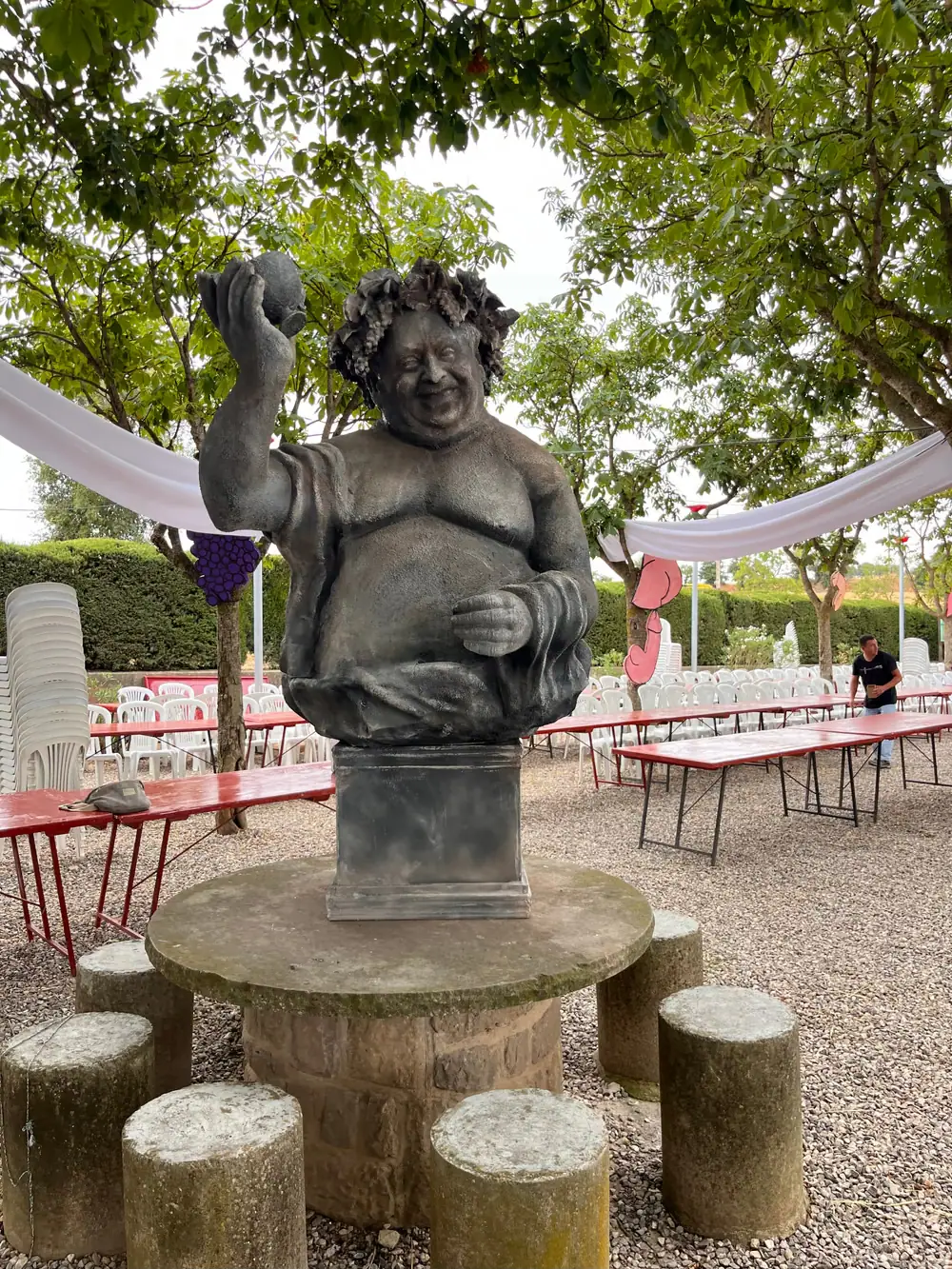 Escultura de Baco con corona de uvas y la mano en alto, sobre una mesa de piedra al aire libre