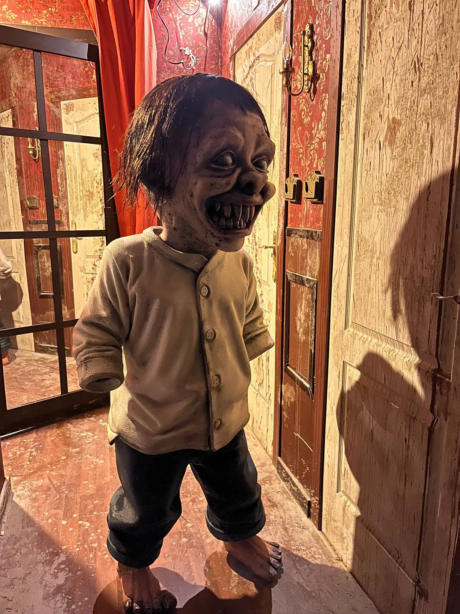 Pasillo de un escape room tematizado de terror, con un niño de dientes afilados y puertas envejecidas