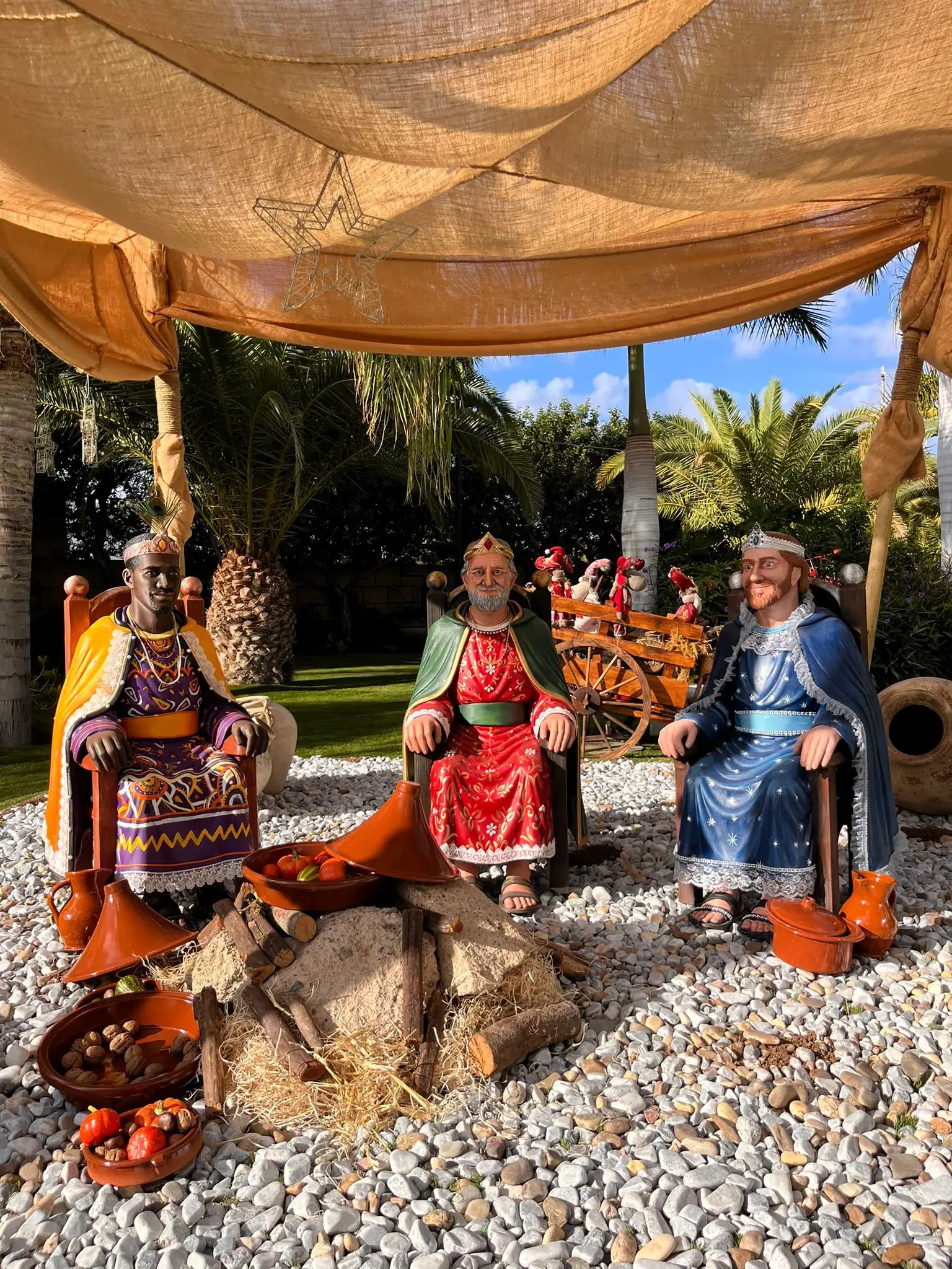 Los tres Reyes Magos en resina a tamaño real, sentados en sus tronos bajo una carpa en un belén al aire libre