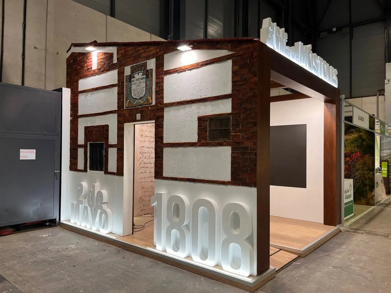 Fachada de ladrillo y vigas de madera en el stand de Móstoles, con las letras 2 de mayo 1808 iluminadas