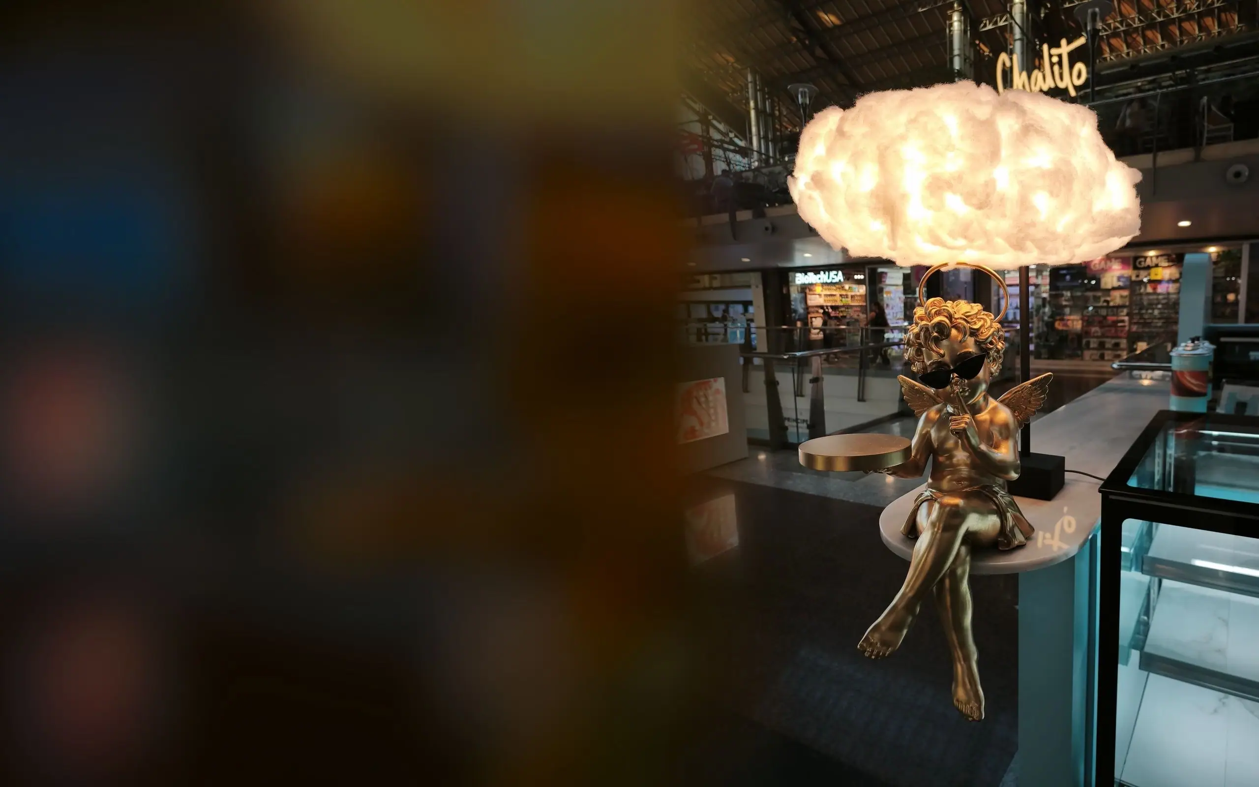 Cupido de resina dorado con gafas de sol bajo una lámpara de nube en un centro comercial