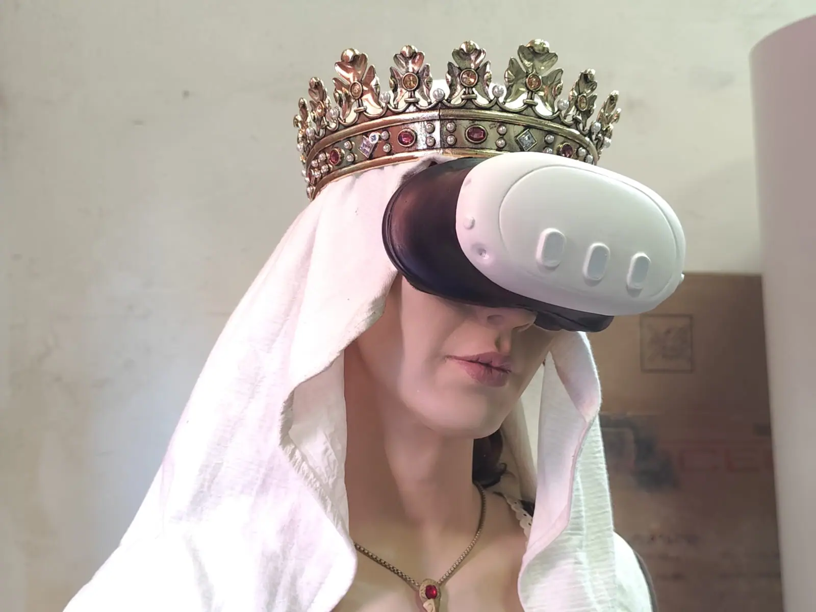 Detalle de la corona, la toca blanca y las gafas de realidad virtual sobre la cara de la figura
