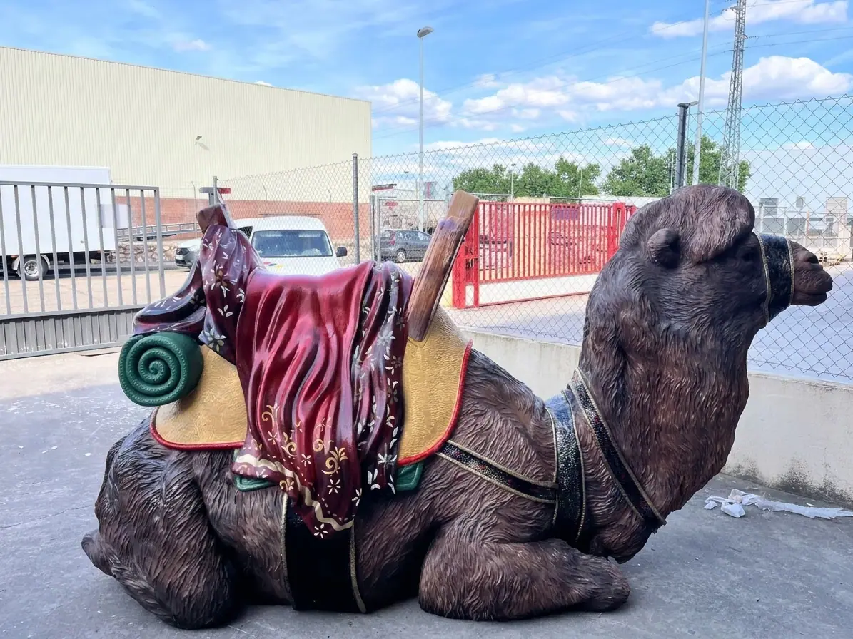 Camello a tamaño real tumbado con montura, manta granate y alfombra enrollada