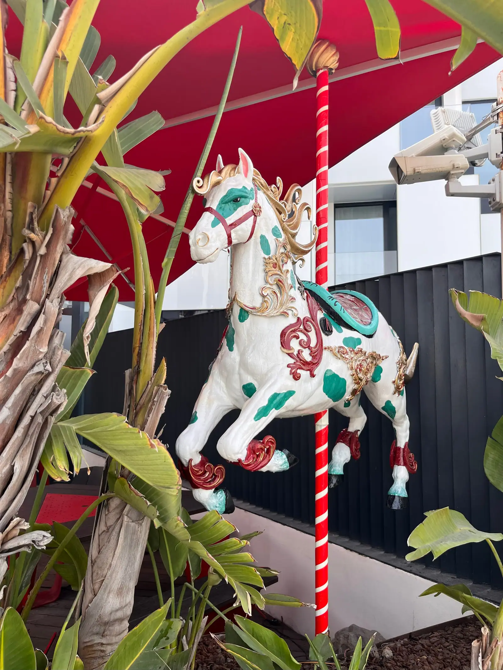 Caballo blanco con flores rojas pintadas a mano, montado en una barra de carrusel entre plantas