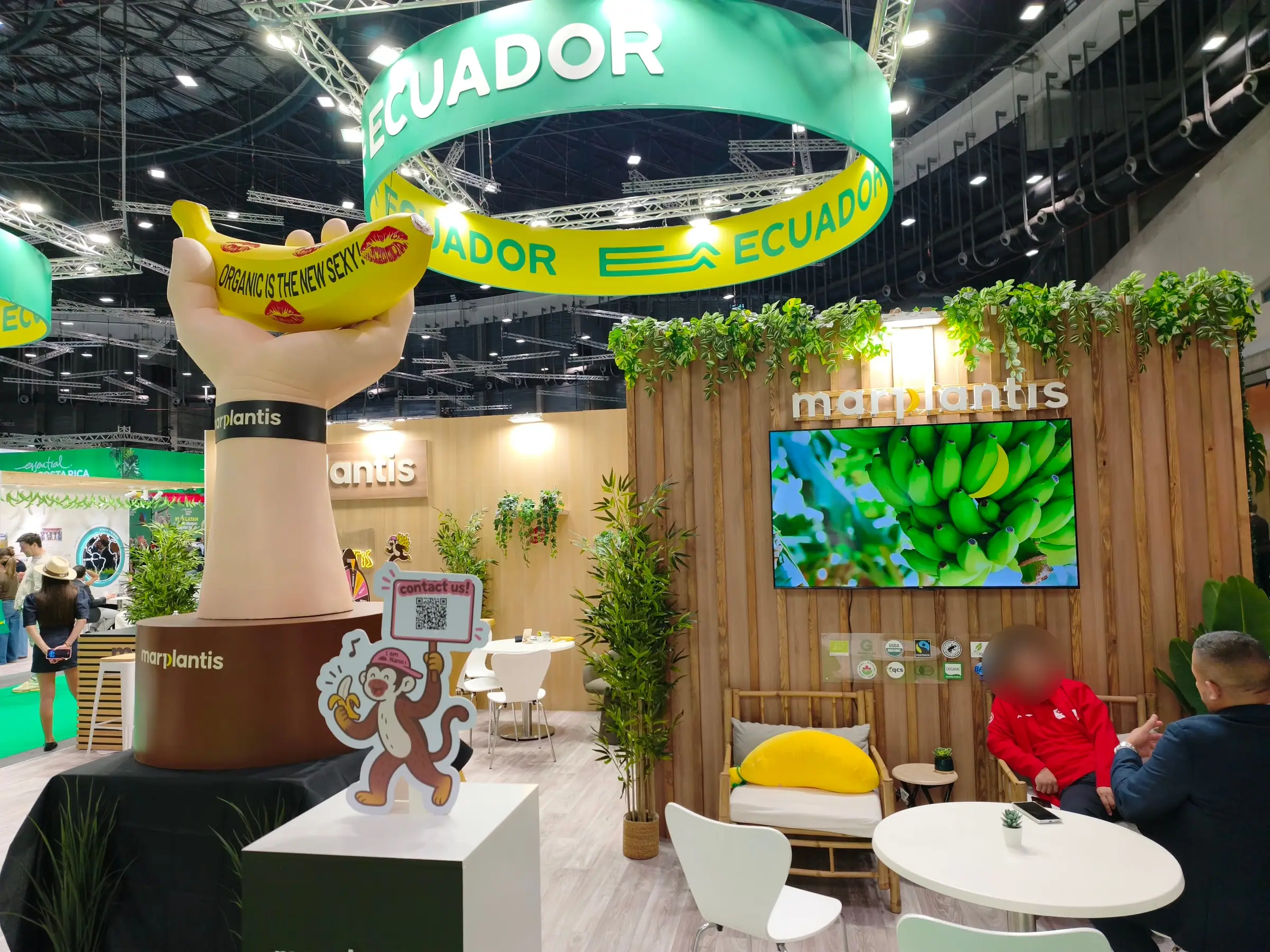 Mano gigante sosteniendo un plátano en el stand de Marplantis, bajo el aro de Ecuador en una feria