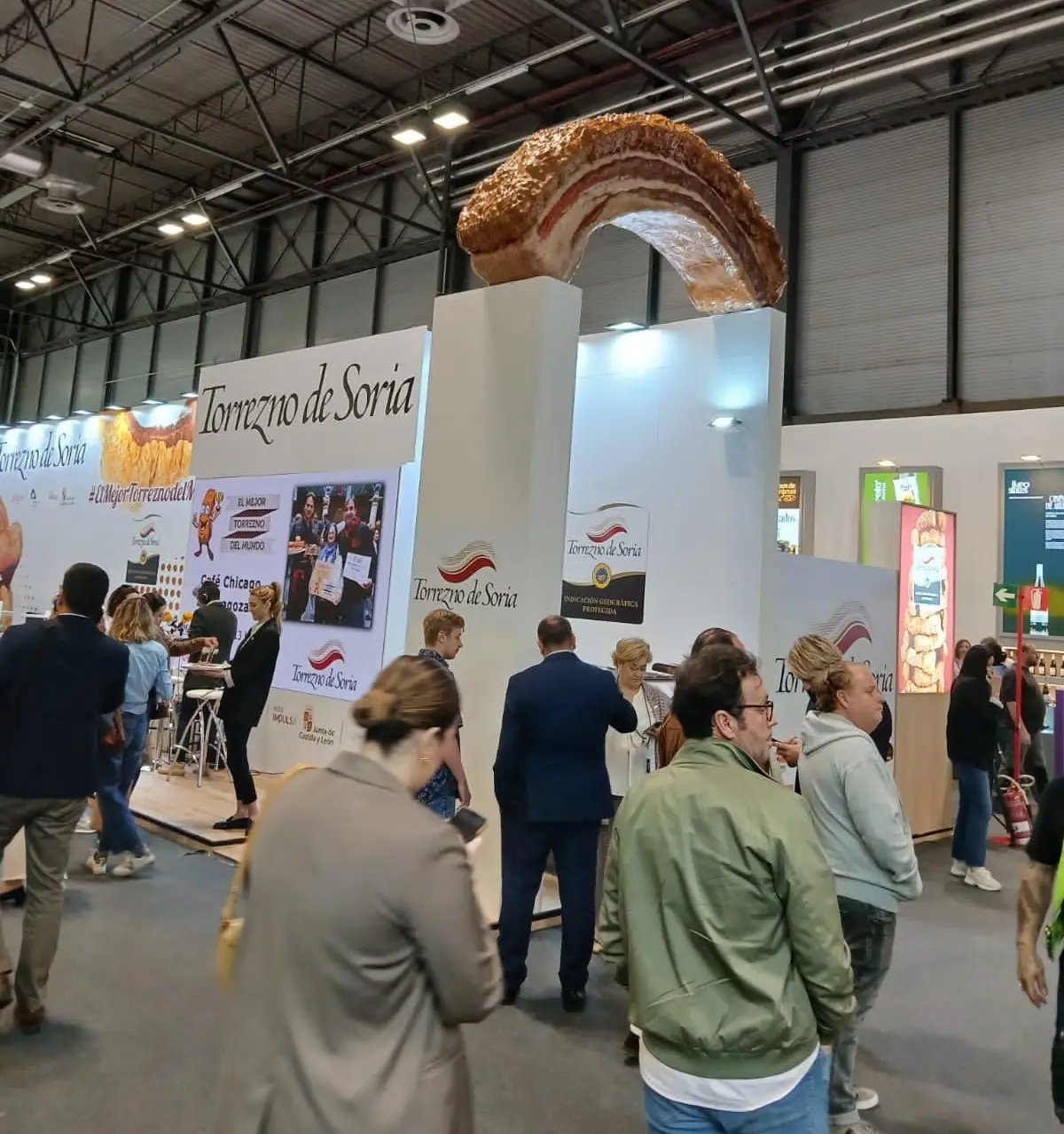 Visitantes de la feria delante del stand de Torrezno de Soria, con el torrezno gigante encima