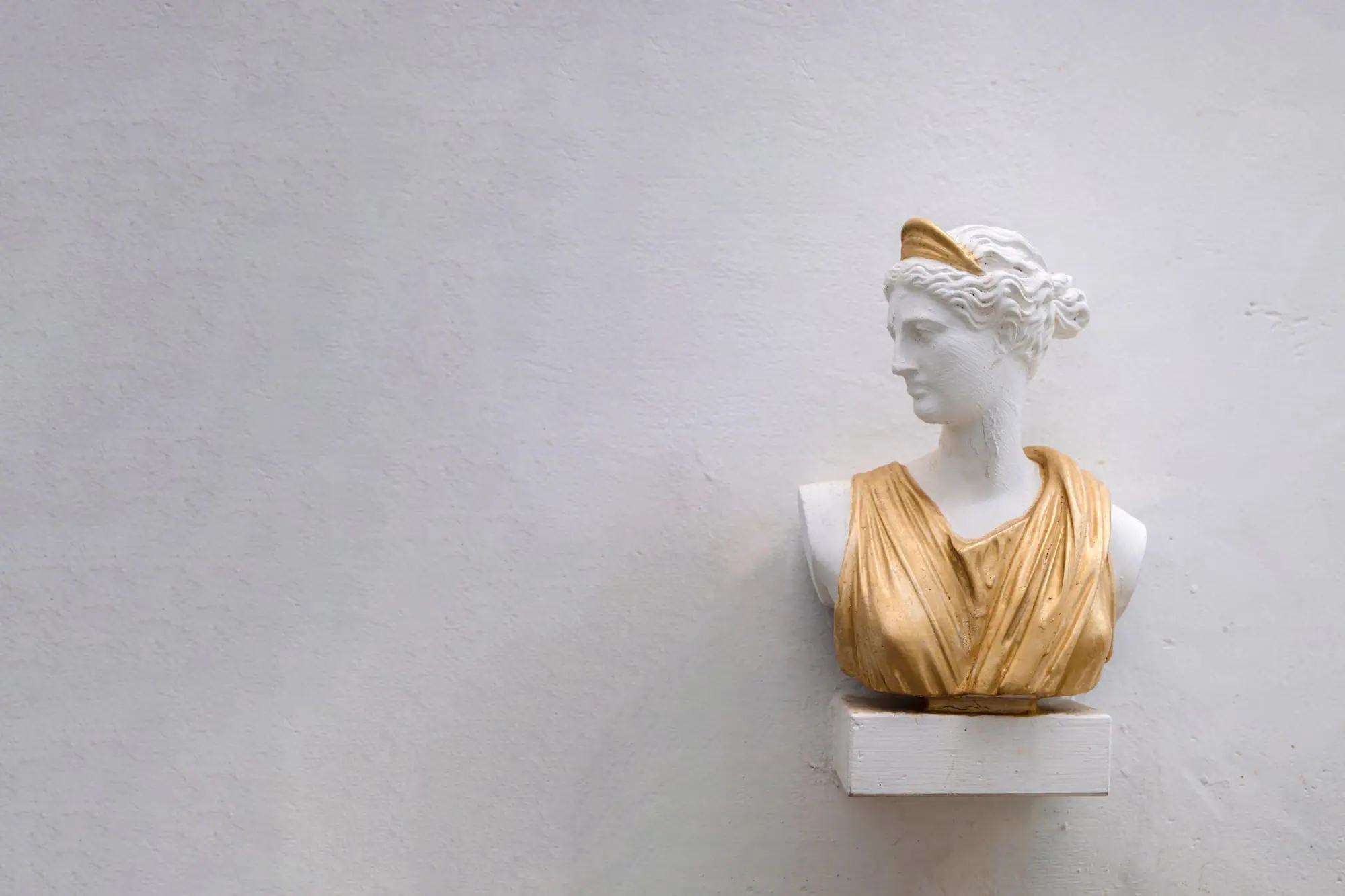 Busto clásico blanco con un drapeado dorado sobre los hombros, colgado en una pared clara