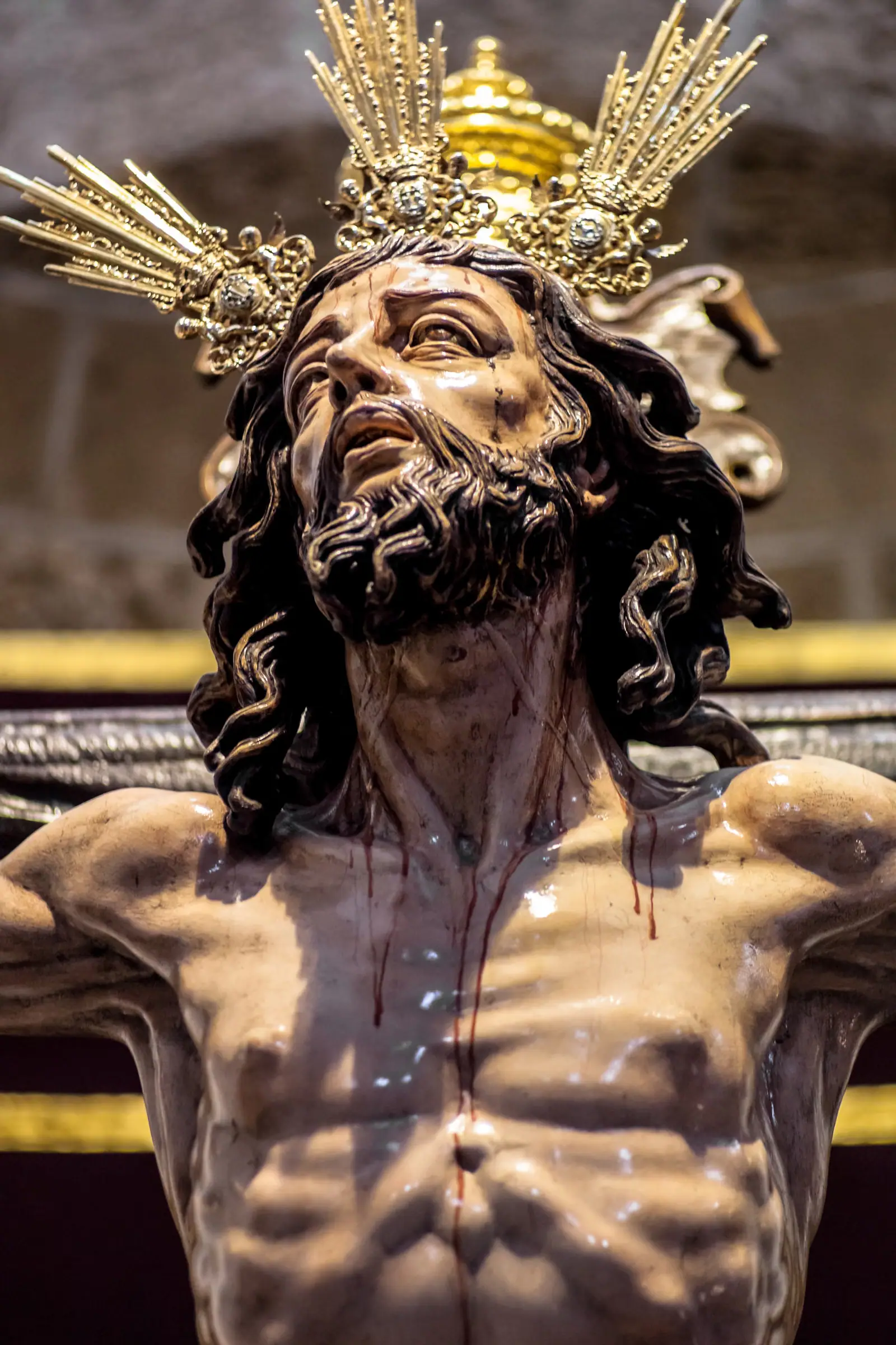 Cristo crucificado policromado mirando al cielo, con potencias doradas y regueros de sangre en el pecho