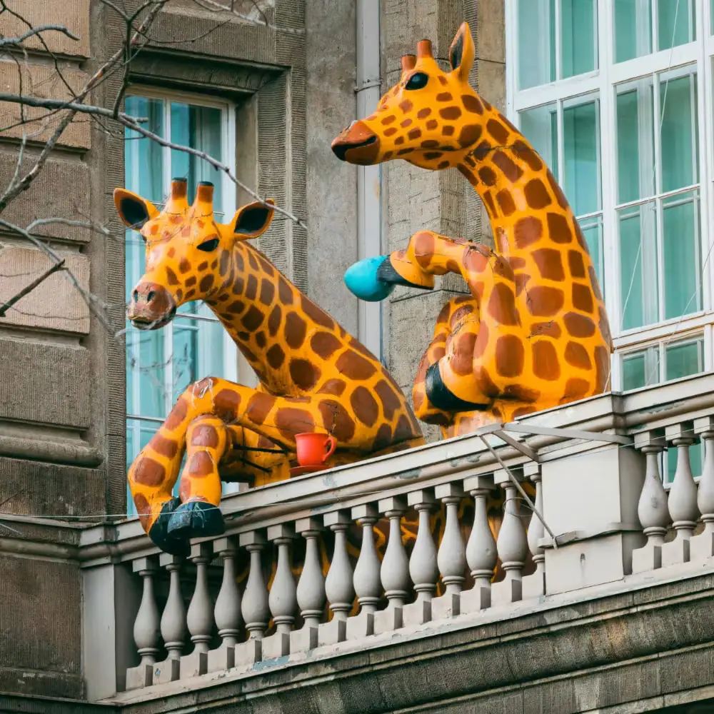 Dos jirafas a tamaño real asomadas a un balcón, una con una taza en la mano