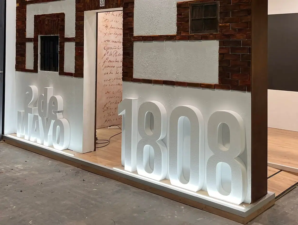Letras y números corpóreos gigantes «2 de mayo 1808» iluminados en un stand de feria