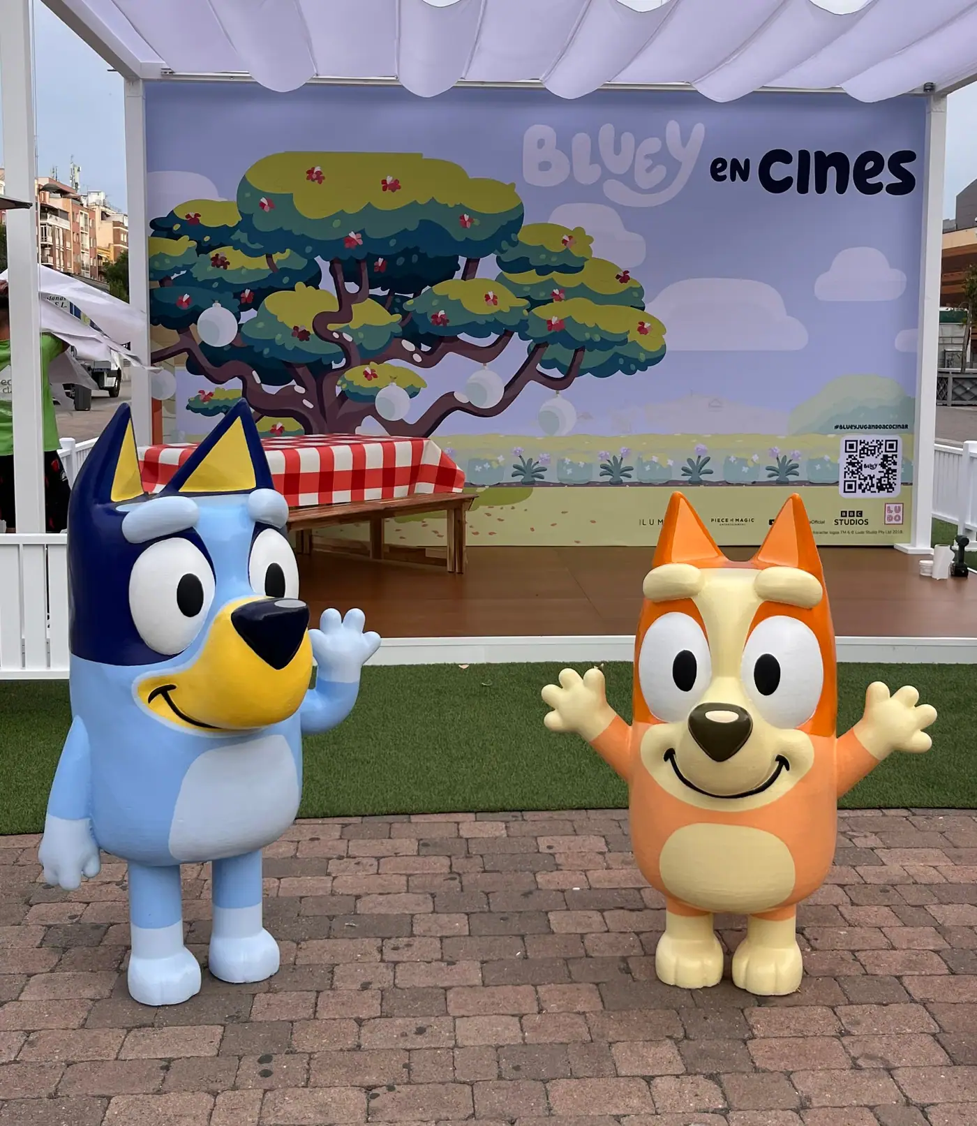 Dos muñecos de fibra de vidrio de personajes infantiles, de pie delante de un photocall en una plaza