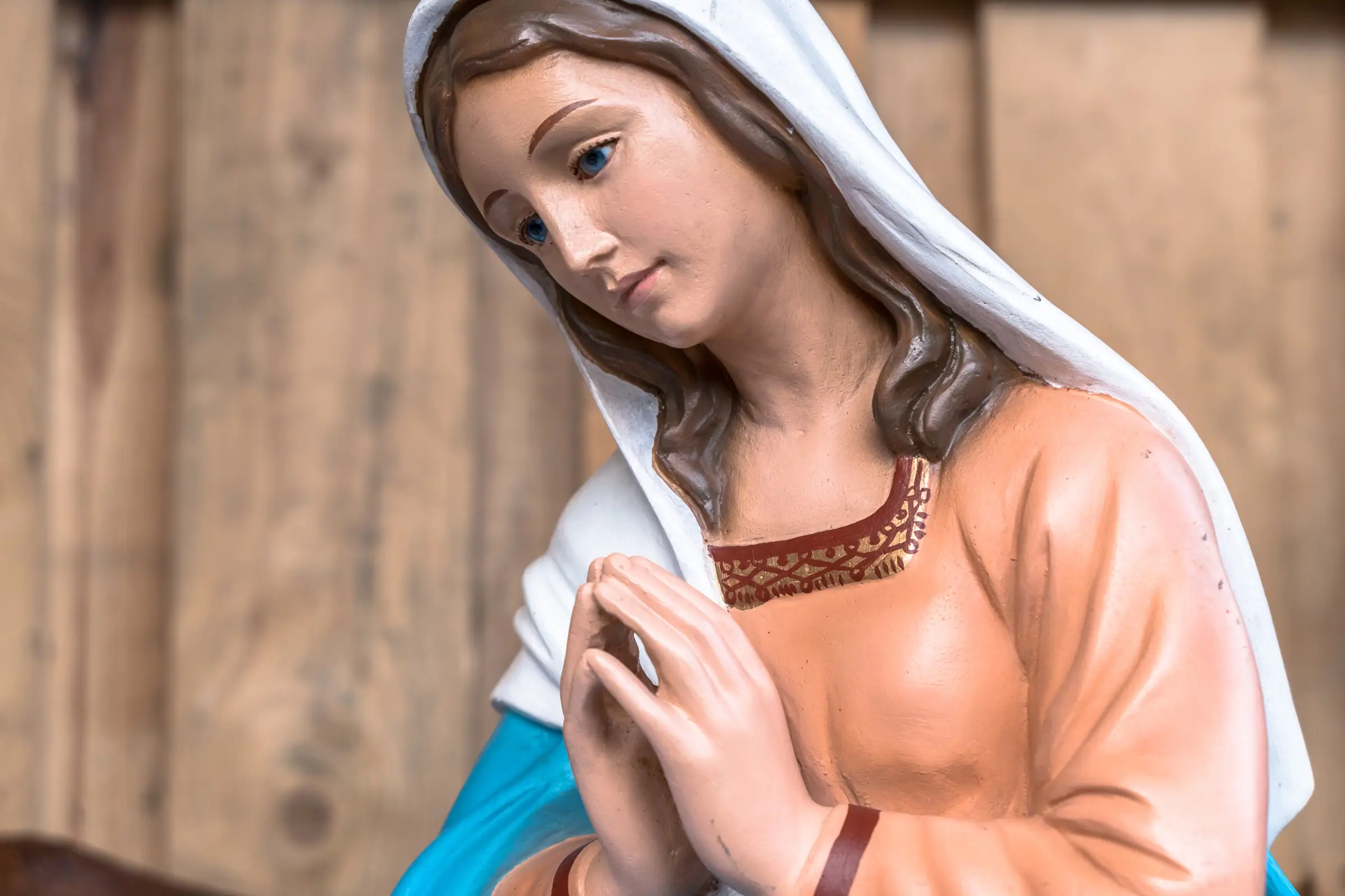 Rostro de una imagen de la Virgen policromada, con manto blanco y las manos juntas en oración